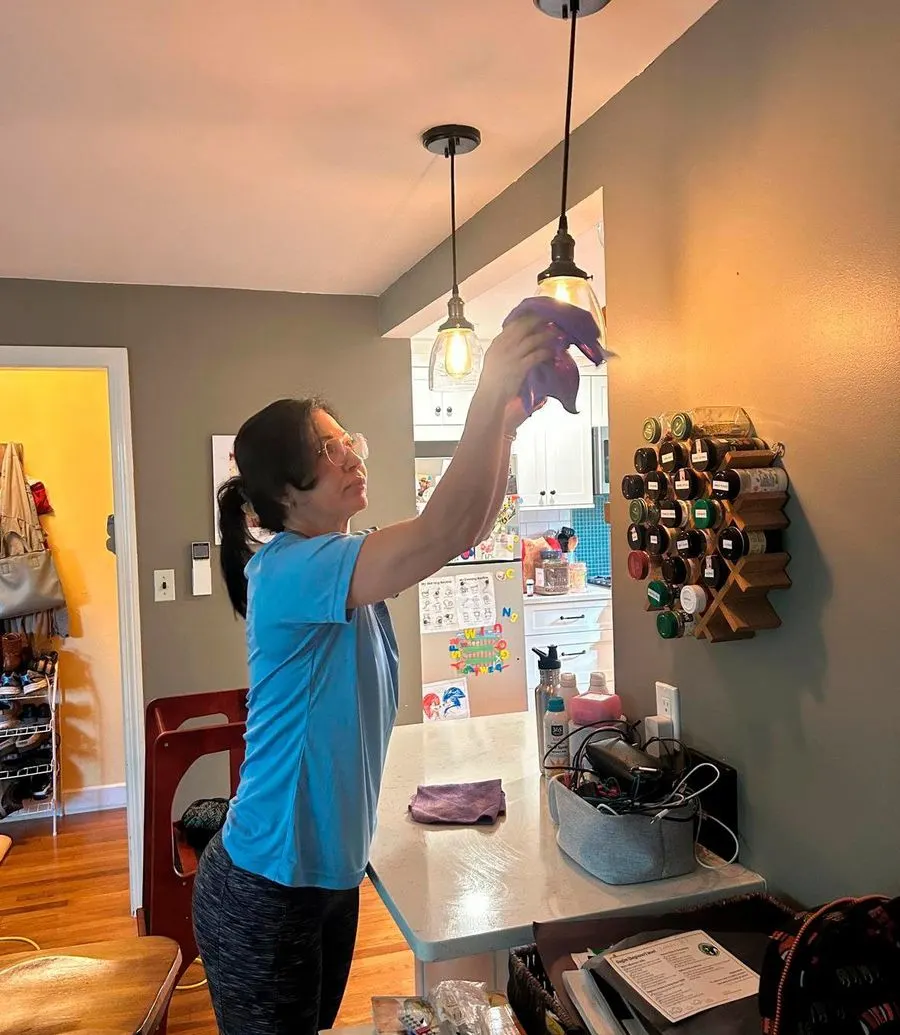 Bedigan cleaner dusting pendant lights over a kitchen counter